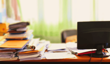 A messy desk with papers, books and a computer monitor