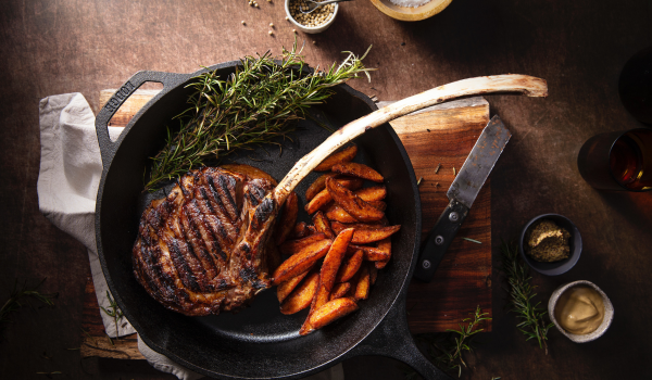 A cast iron skillet with a tomahawk steak, steak fried potatoes and asparagus